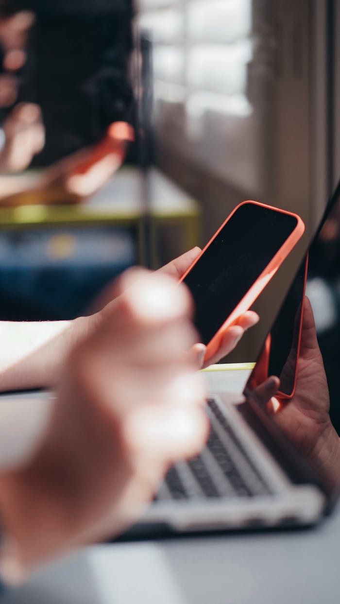 about-02 Hands holding smartphone near laptop, showcasing multitasking and technology use.